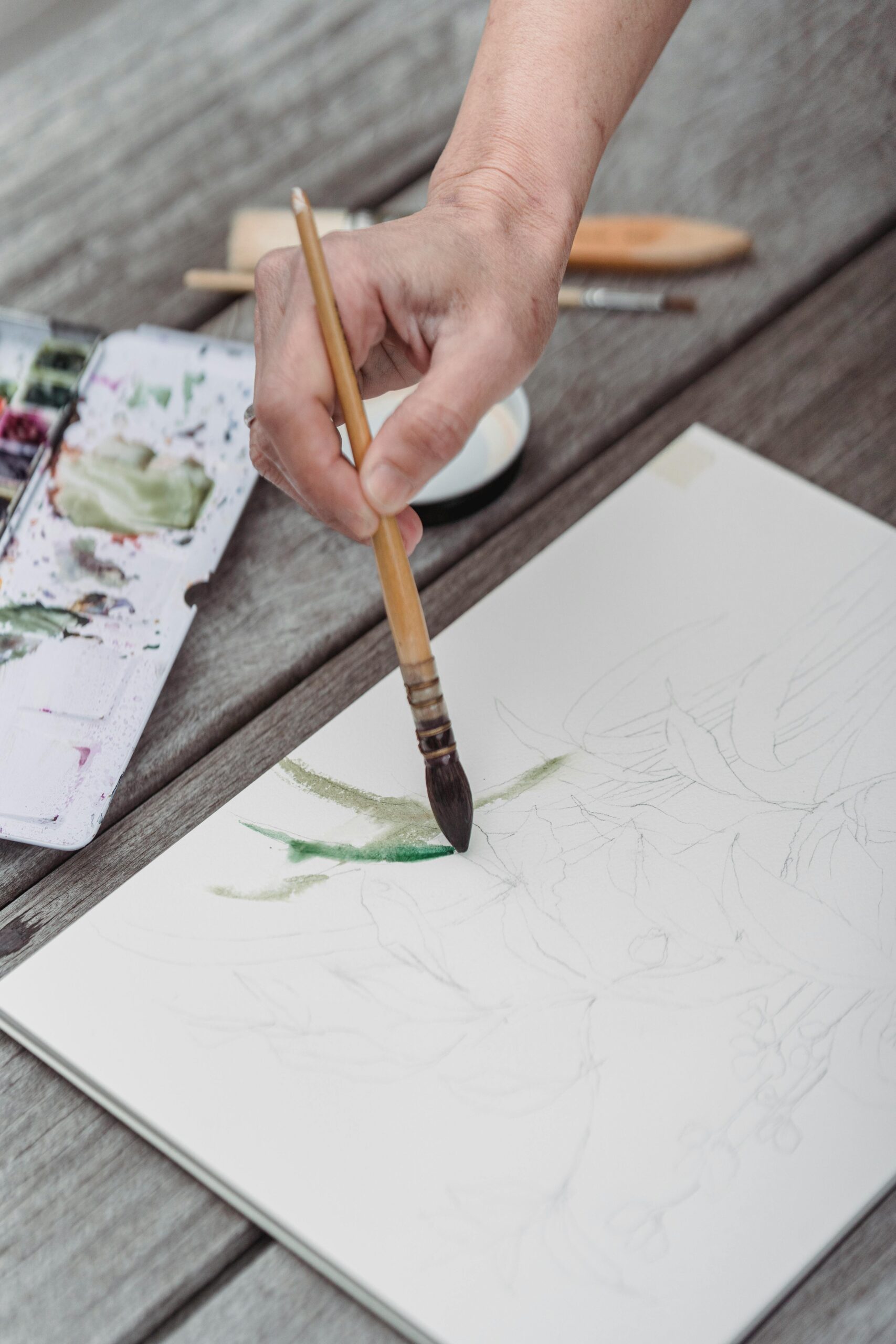 A hand delicately paints with watercolors on a sketchpad, showcasing artistic expression.